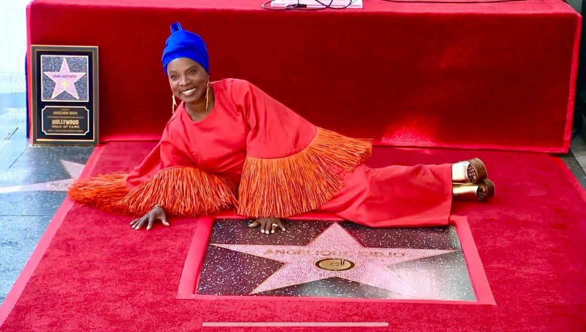 Angélique Kidjo, en robe rouge à franges et turban bleu, allongée sur le tapis rouge auprès de son étoile du Hollywood Walk of Fame