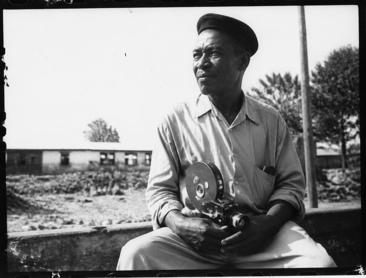 Portrait en noir et blanc d'un cinéaste sénégalais assis avec une caméra 16 mm